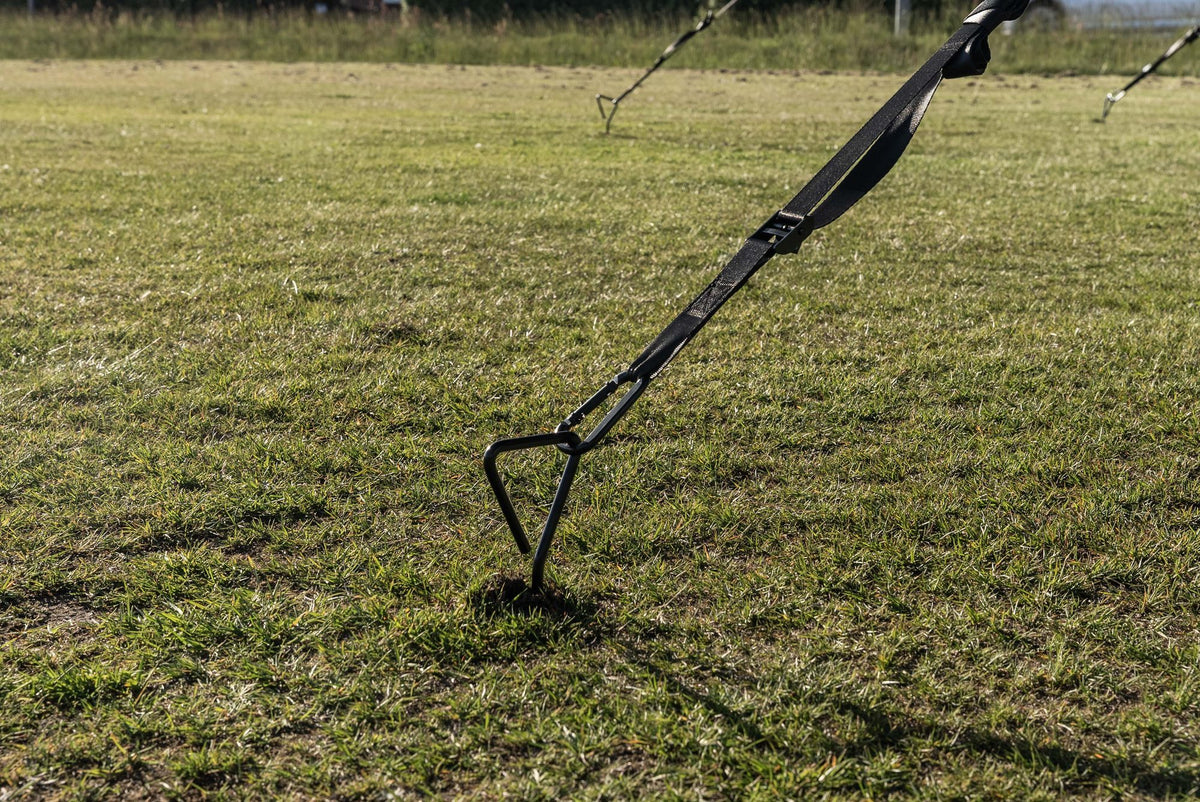 A ground anchor screwed into the grass and tensioned with the storm strap