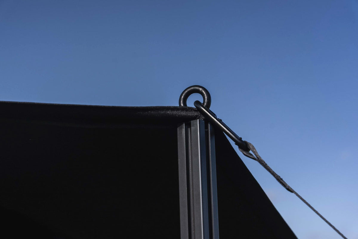 The sail's corner on top of the support pole, with carabiner and strap against a blue sky
