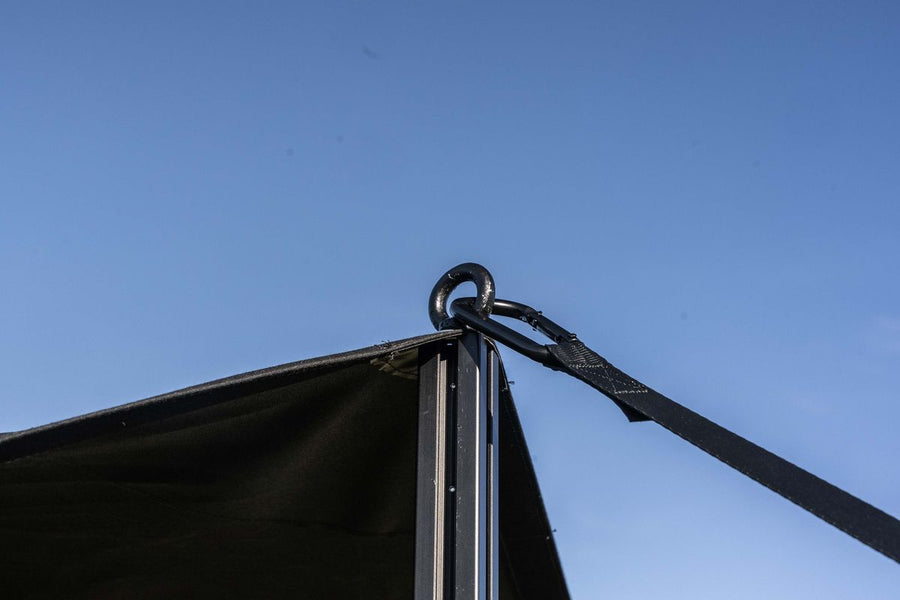 The sail's corner on top of the support pole, with carabiner and strap against a blue sky